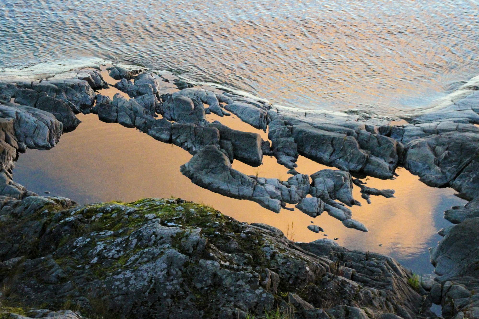 Golden hour magic, orange soft sunrise light with reflections on cliff at rocky sea shore in Sweden.